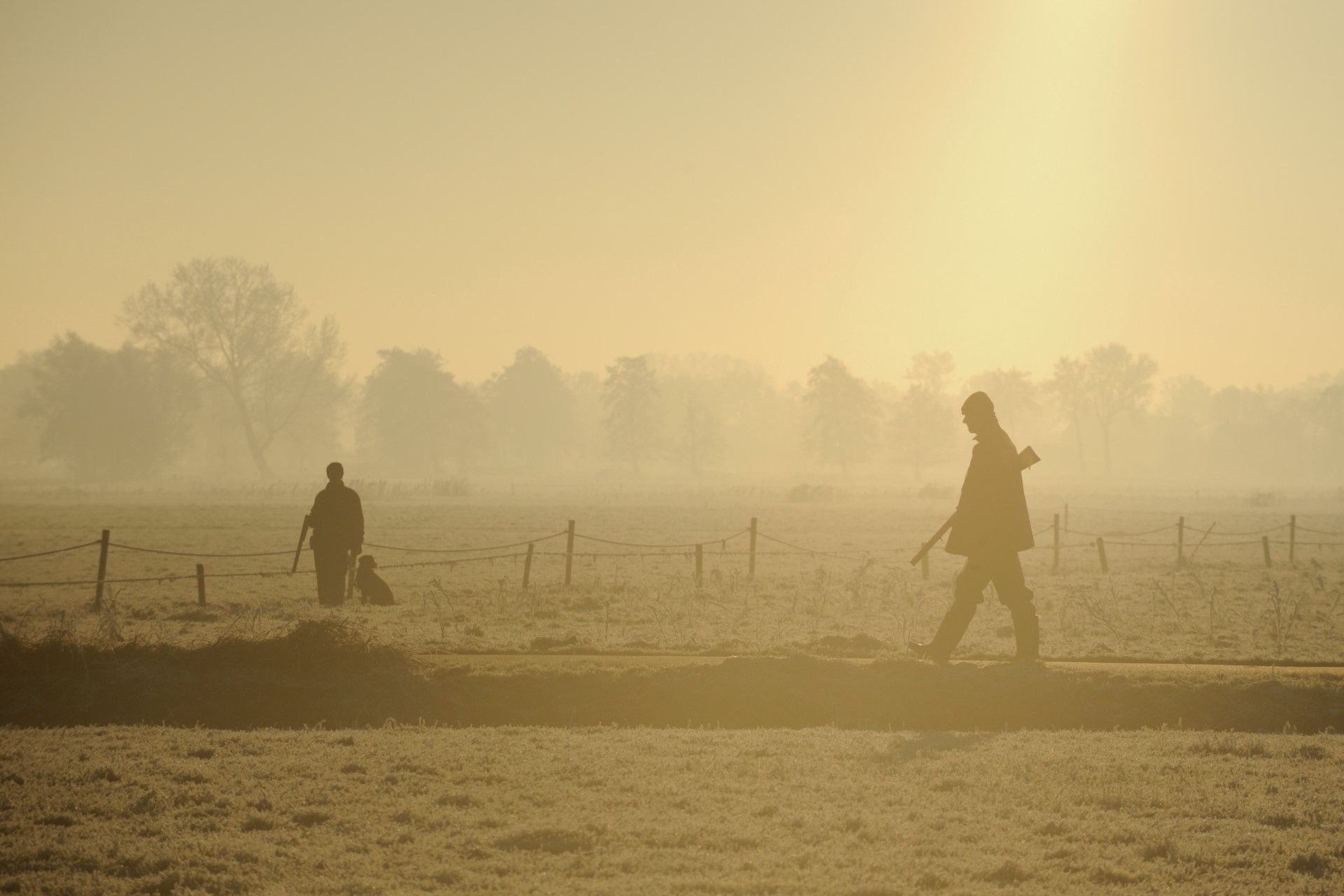 Foto van twee jagers met een jachthond in de ochtendmist.